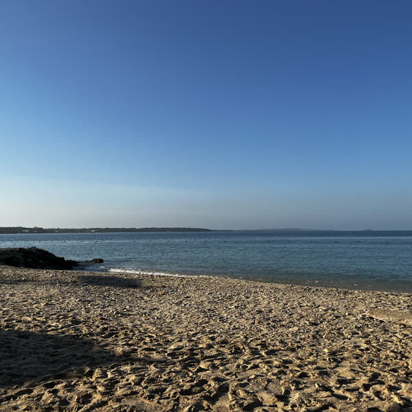 A wide empty sandy beach under a clear blue sky